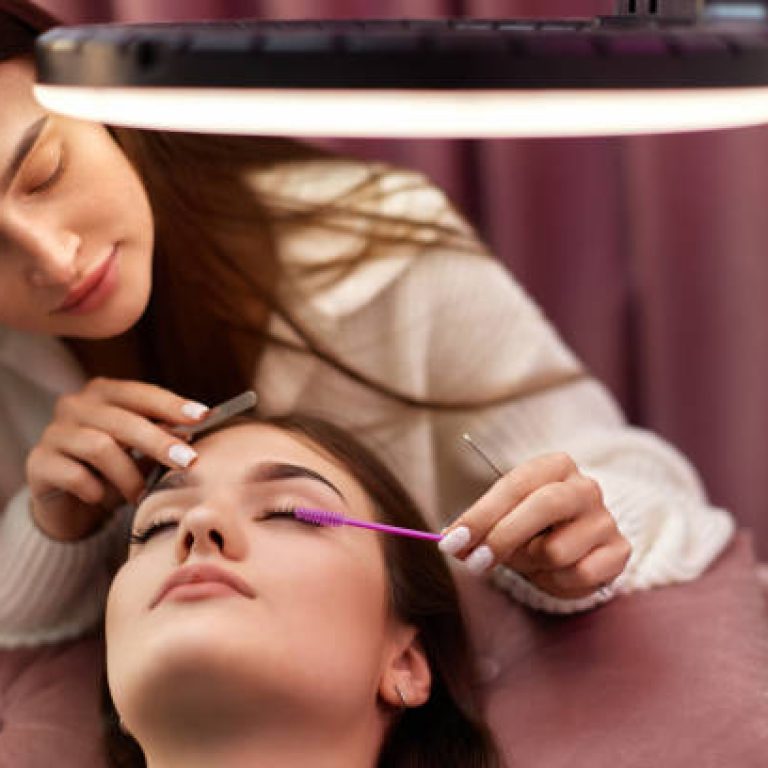 master using brush for combs the eyelashes of the client after the eyelash extension procedure. Cosmetology
