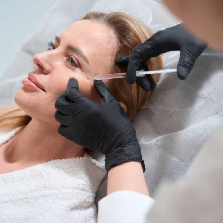 Female blonde gets a rejuvenating injection in her cheeks, an esthetician uses a thin needle