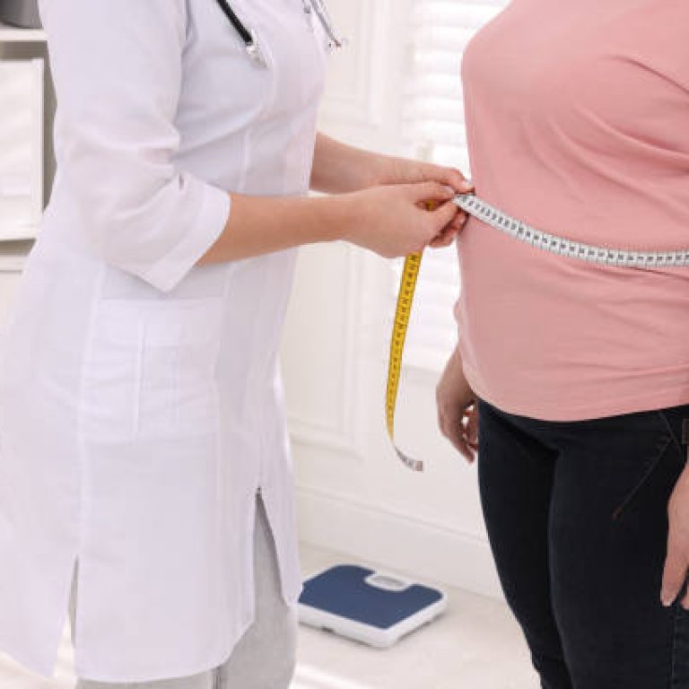 Nutritionist measuring overweight woman's waist with tape in clinic, closeup