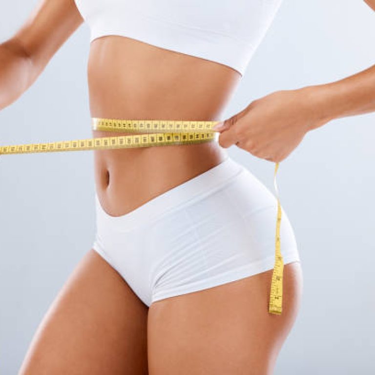 Weightloss, health and woman with measuring tape in a studio for her diet, exercise or wellness. Fitness, body and healthy slim female model checking the measurement of her waist by a gray background